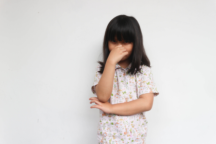 Little girl kid wearing pajama smelling something stinky and disgusting, intolerable smell, holding breath with fingers on nose. bad smell