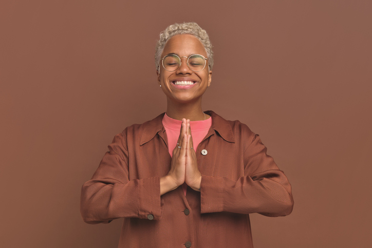 Young happy African American woman folding palms for prayer closes eyes
