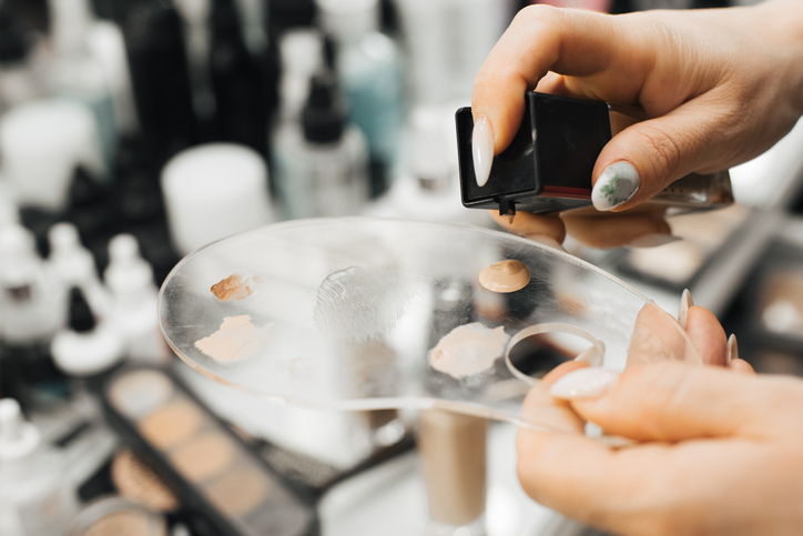 A woman's hand holds a palette and squeezes a cosmetic product, a foundation, onto it. close-up