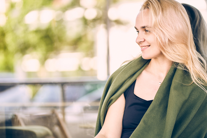 Woman in green blanket is sitting in the outdoor cafe and smiling on the background of window glass. The concept of blind date and dreaming.