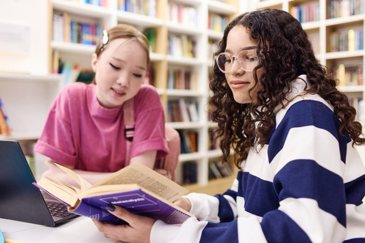 Girl Wearing Glasses Reading Book in Library with Friends