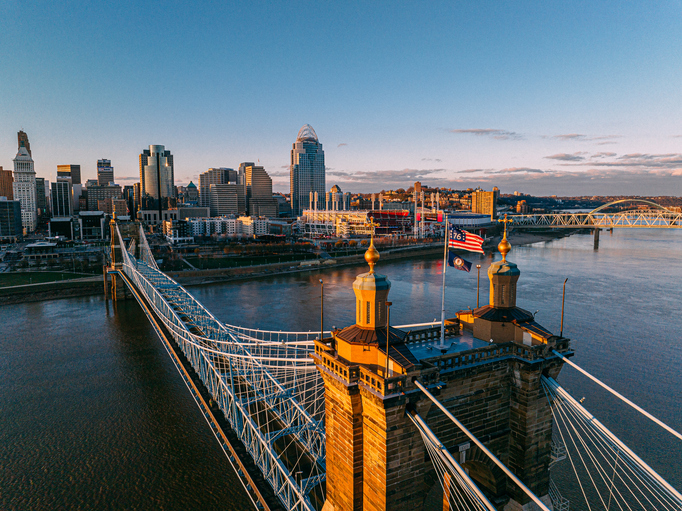 High Angle View of The Bennington 76 flag and Commonwealth of Kentucky Flag Flying on the John A. Roebling Bridge with Downtown Cincinnati Along the Ohio River