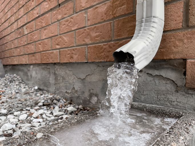 Frozen Downspout Water Turned Into Ice Outside Brick House on Cold Winter Day Closeup