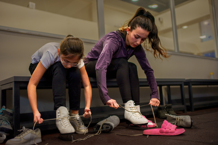 Ice Skating Lesson: Instructor andYoung Girl tying ice skate shoelaces close up