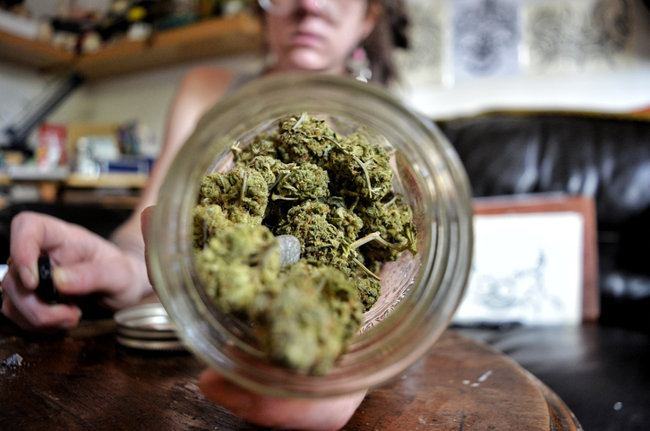 Midsection Of Woman Holding Marijuana In Jar On Table