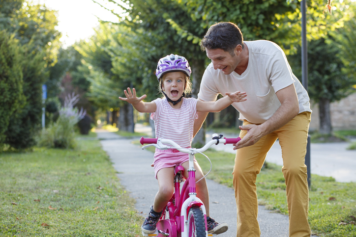 Little girl learning how to ride a bike with help of her father