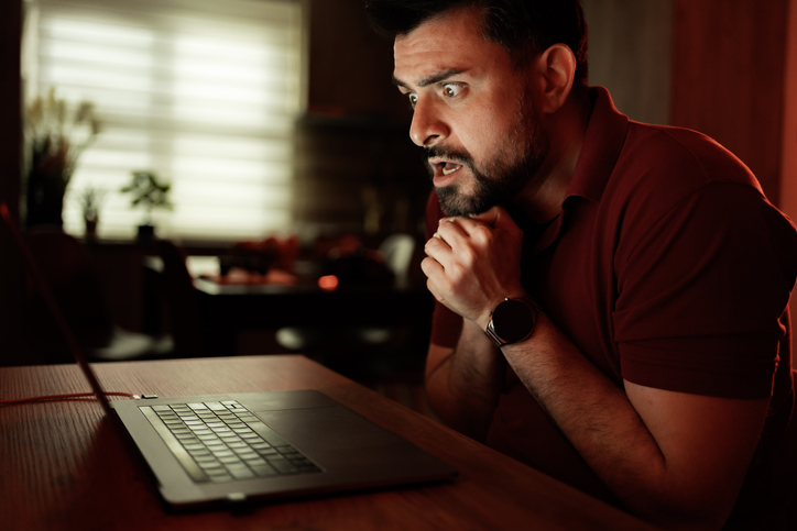 Shocked man looking at laptop screen at night at home