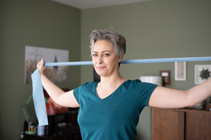 Middle aged woman doing stretching exercises with blue stretch band or gymnastic band