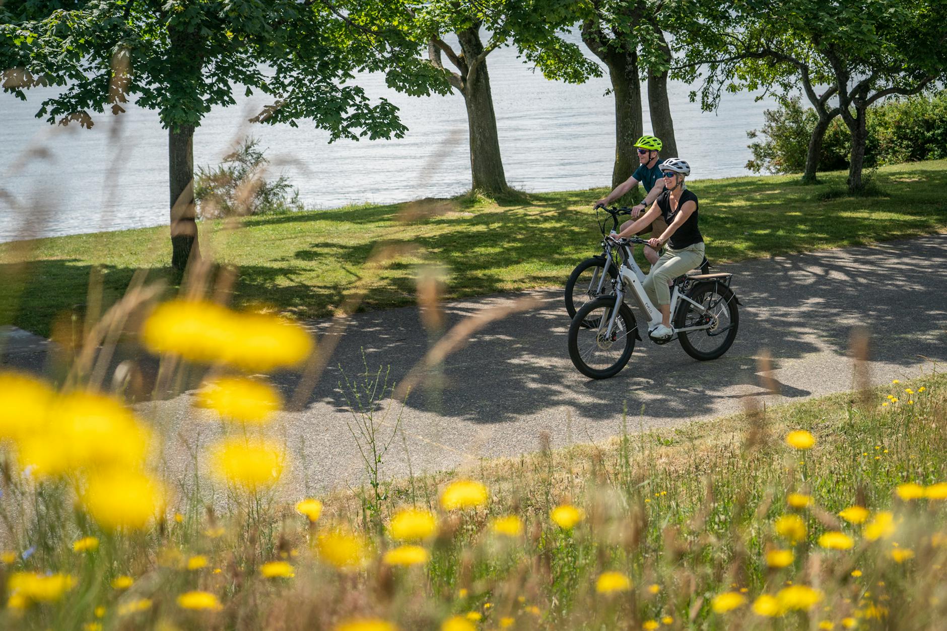 a couple wearing helmets riding electric bikes on road near lake
