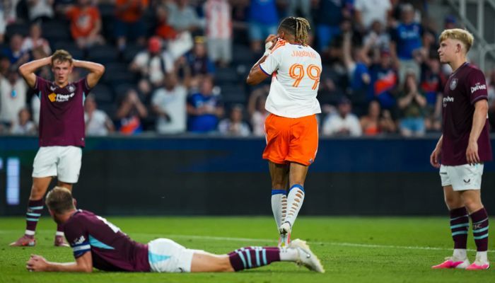 A soccer player in an orange jersey falls to the ground after a collision with an opposing player in a dark jersey.