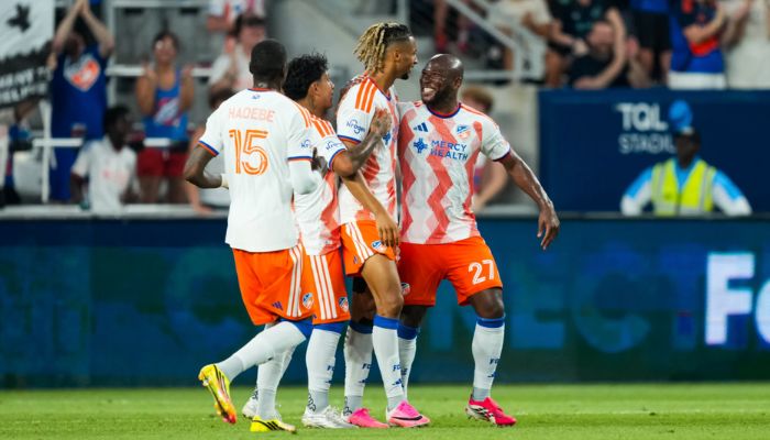 Soccer players in orange and white jerseys celebrating on a soccer field.