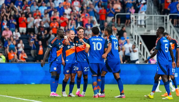 A group of soccer players in blue uniforms celebrating together on a soccer field.