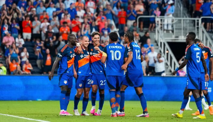 A group of soccer players in blue uniforms celebrating together on a soccer field.