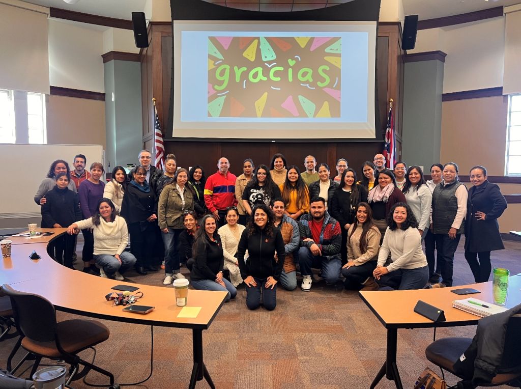 A group of people gathered in a room, with the text "gracias" displayed on a projection screen behind them.