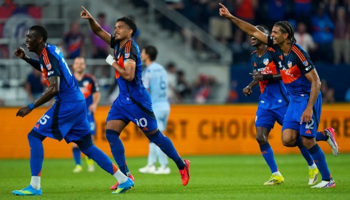 Soccer players in blue uniforms celebrating a goal on a soccer field.