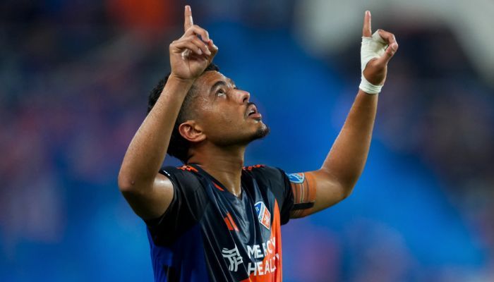 A soccer player in a black jersey raising both arms in celebration on a blue field.