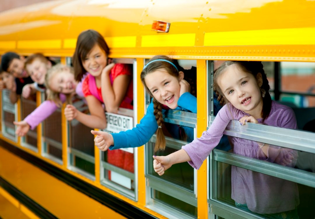 A group of smiling children looking out of the windows of a school bus.