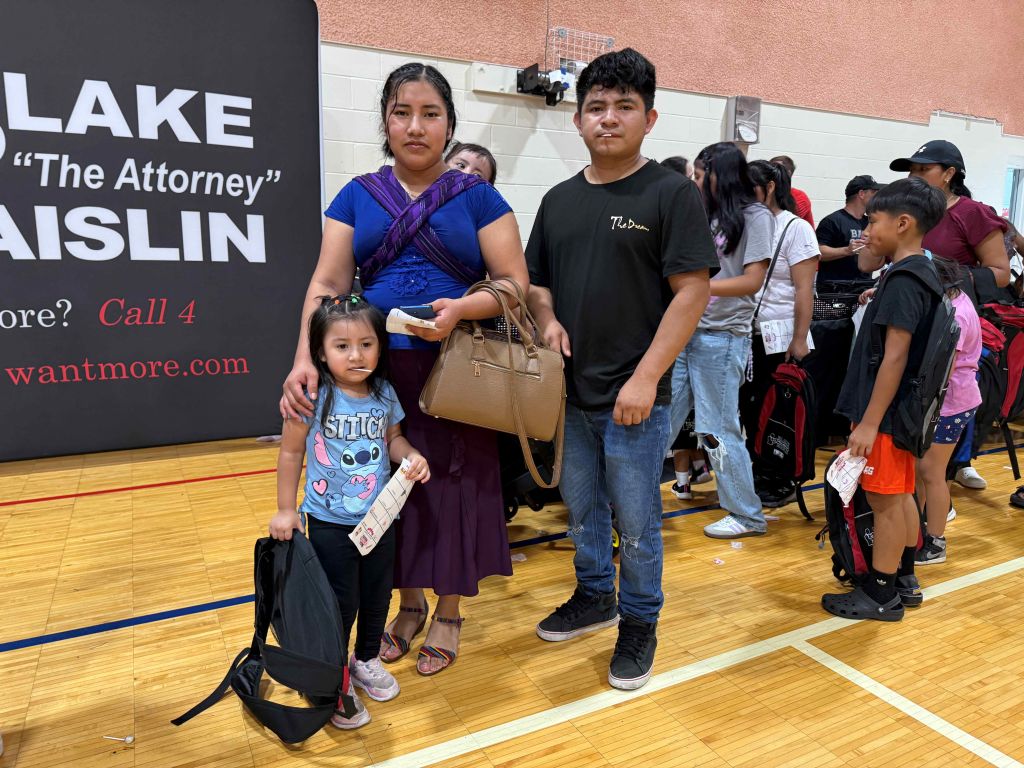 A group of people, including a woman and a young girl, standing in front of a sign for "LAKE 'The Attorney' AISLIN" advertising legal services.
