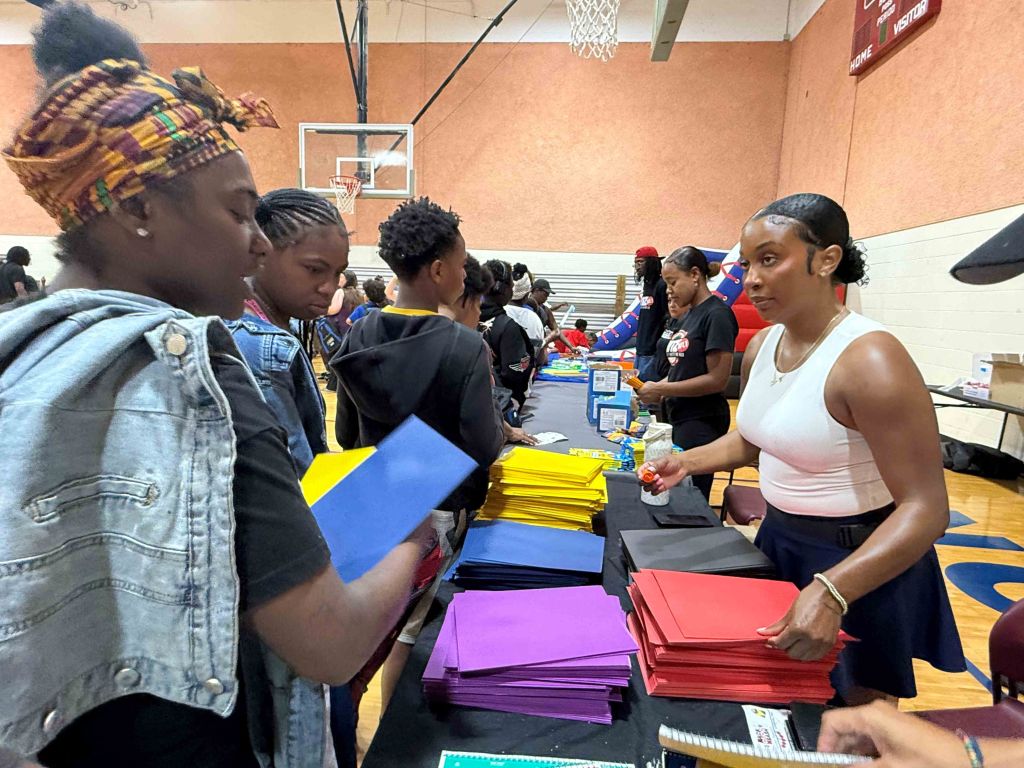 A group of young people gathered in a basketball court, examining and organizing various school supplies and materials.