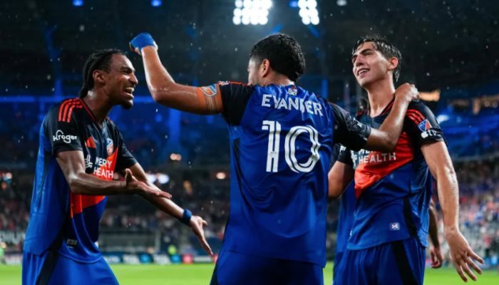 Three soccer players celebrating on a field, with one player's jersey displaying the name "Evanser".